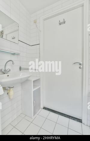 Lavabo en céramique blanc et miroir sur le mur à côté de la porte d'entrée d'une salle de bains Banque D'Images