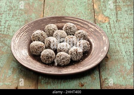 Bonbons végétaliens crus faits maison dans des copeaux de noix de coco en plaque de céramique sur une vieille table en bois Banque D'Images