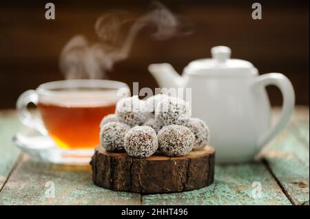 Bonbons végétaliens faits maison dans des copeaux de noix de coco servis avec un foyer sélectif de thé noir chaud à la vapeur Banque D'Images