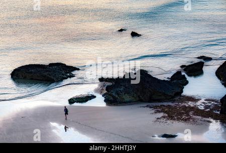 Cornouailles,Angleterre-juillet 21 2021:à Carneas à Bedrithan, une figure humaine marche le long des sables humides, parsemés de grandes roches, en milieu d'été, silhoueté par Banque D'Images