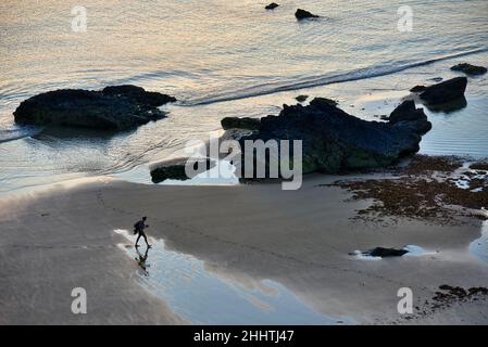 Cornouailles,Angleterre-juillet 21 2021:à Carneas à Bedrithan, une figure humaine marche le long des sables humides, parsemés de grandes roches, en milieu d'été, silhoueté par Banque D'Images