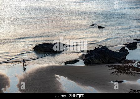 Cornouailles,Angleterre-juillet 21 2021:à Carneas à Bedrithan, une figure humaine marche le long des sables humides, parsemés de grandes roches, en milieu d'été, silhoueté par Banque D'Images