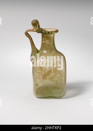 Flacon en verre 1st–3rd Century A.D. Roman petit flacon carré à poignée unique.Vert jaune translucide; manche de même couleur.rebord replié, rond et intérieur et pressé sur les côtés de la bouche; col cylindrique, extensible vers le bas; épaulement incliné; corps carré avec côtés irréguliers et coins inférieurs arrondis; fond plat;Poignée à deux nervures fixée à l'épaule, orientée vers le haut et vers l'extérieur, tournée horizontalement, et tractée sur le bord extérieur de la jante avec boucle au-dessus.d'un côté, motif en relief ressemblant à des lettres et lignes en relief plus évanouissement sur les deux autres côtés; en bas, motif carré en relief, flanqué sur Banque D'Images