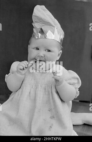 Bébé portant un chapeau de fête et manger un doigt de chocolat Cadbury 31 Octobre 1952 Banque D'Images