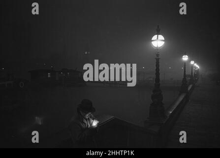 Un homme allume une cigarette sur le quai de la Tamise la nuit.Vers 1955. Banque D'Images