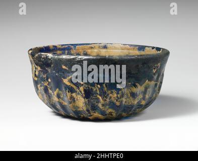 Bol en verre à côtes fin du 1st siècle C.-B.–début du 1st siècle A.D. Roman bleu cobalt translucide.bordure légèrement arrondie écartée;Côtés profonds avec bande lisse autour du haut, courbé vers le bas légèrement concave.à l'intérieur, une large rainure horizontale sous le bord, et deux étroites rainures incurvées de près coupées dans une bande autour du milieu du corps; à l'extérieur, vingt-cinq longues, peu profondes, nervures verticales,Dépouille vers le bas et s'étendant jusqu'au bord du fond.intact, mais quelques fissures internes; bulles de piquer; morcellement, iridescenence de briiliant, et des morceaux de l'épais crémeux intempéries.marques de meulage rotatif à l'intérieur et Banque D'Images