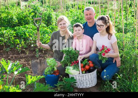 Famille gaie tenant des légumes cultivés dans le jardin à la maison Banque D'Images