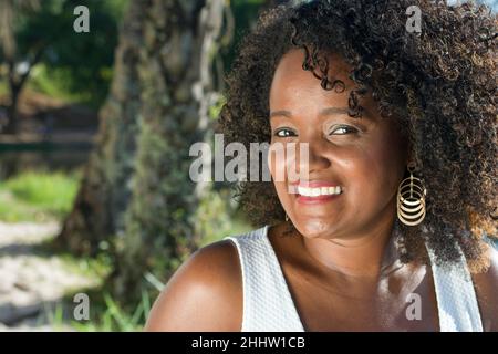 Magnifique modèle en robe blanche souriant et regardant l'appareil photo.En arrière-plan arbres, plantes, fleurs et la rivière dans le paysage.Salvador, Bahia Banque D'Images