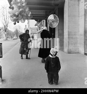 Une femme qui vend des ballons à Vienne.Pendant des heures, la vieille dame de Vienne avait piétiné les rues froides de l'hiver en essayant de vendre ses marchandises volant d'une corde attachée à sa ceinture.Enfin, elle a fait une vente, et un client très content est parti avec sa capture volant d'une corde attachée à un bouton sur sa côte.Le plaisir sur son visage et le plaisir sur le visage de la vieille femme valait la peine d'attendre.Vienne, Autriche.Février 1954. Banque D'Images