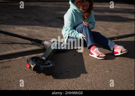 Une femme de race blanche est tombée d'un scooter électrique et a blessé sa jambe.Souffrant de douleur. Banque D'Images