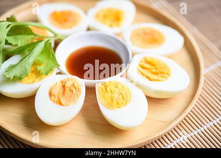 Œufs petit-déjeuner, menu d'œufs frais aliments œufs durs dans une assiette en bois décorée de feuilles de céleri vert et de sauce de poisson sur fond de bois, coupé en deux Banque D'Images