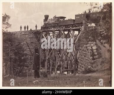 Pont sur Orange et Alexandria Rail Road,Tel que réparé par les ingénieurs de l'armée sous le colonel Herman Haupt 1865 Andrew Joseph Russell American ce point de vue de Russell documente le moteur Fire Fly testant la stabilité d'un nouveau pont en bois construit rapidement par les ingénieurs du chemin de fer militaire des États-Unis pour remplacer un pont de maçonnerie détruit par les Confederates.Au-dessus du wagon-caisse qui suit le moteur se trouve une paire de passages armés; d'autres sont sur les rails et la fondation du pont.La figure hante au premier plan n'est pas identifiée, mais il peut être le photographe lui-même ou un chemin de fer civil Banque D'Images