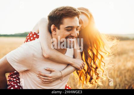 Portrait en gros plan couple d'homme et de femme jouant à l'extérieur dans un champ ouvert, pigeback tour. Banque D'Images