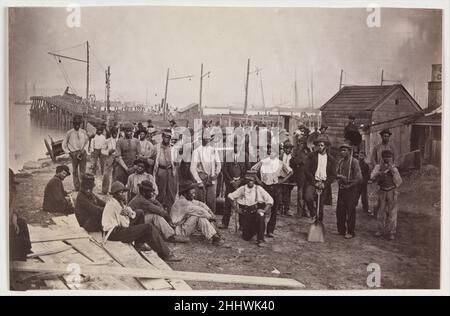 Ouvriers à Quartermaster's Wharf, Alexandria, Virginie 1863–65 attribué à Andrew Joseph Russell American le bureau de Quartermaster des États-Unis a géré l'approvisionnement, l'entreposage et la distribution de nourriture, de carburant, d'ordnance, de fournitures médicales, de fourrage pour les animaux,et même la livraison de courrier pour l'armée.Cette vue extraordinaire montre un groupe d'esclaves émancipés qui ont travaillé comme ouvriers payés pour l'armée le long de l'immense ensemble de quais à Alexandrie, en Virginie.L’un des freedmen tient une place de charpentier, l’un un le baril, les autres pelles à charbon portant les initiales de l’Armée des États-Unis.Les travailleurs se moque Banque D'Images