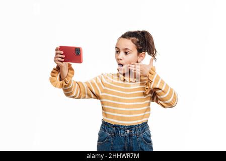 Fille prenant un selfie avec un téléphone portable tout en se tenant sur un fond blanc isolé. Banque D'Images