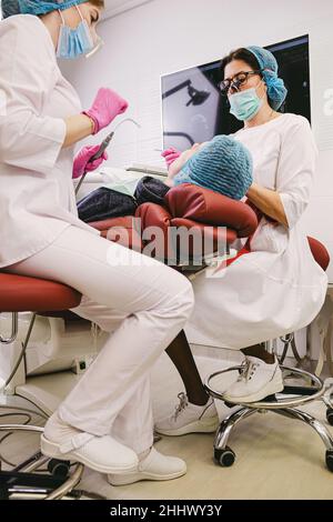 Les dentistes travaillent dans une clinique moderne de stomatologie avec un assistant utilisant des instruments stomatologiques faisant la procédure de guérison des dents à un patient Banque D'Images