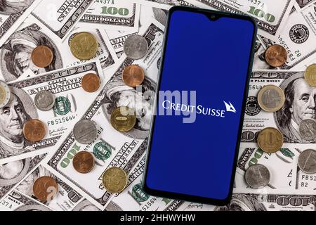 Smartphone avec logo de la banque Credit Suisse entouré d'une variété de pièces de monnaie en métal sur fond de billets en dollars Banque D'Images