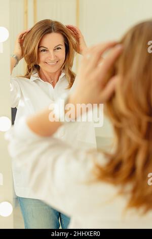 Portrait d'une belle femme souriante devant un miroir.Race blanche blonde positive.Tir vertical Banque D'Images