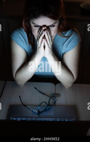 une femme fait des heures supplémentaires.Un étudiant étudiant étudiant étudiant à un ordinateur portable la nuit dans l'obscurité.La jeune fille s'inquiète des problèmes au travail et tient ses mains sur son visage. Banque D'Images