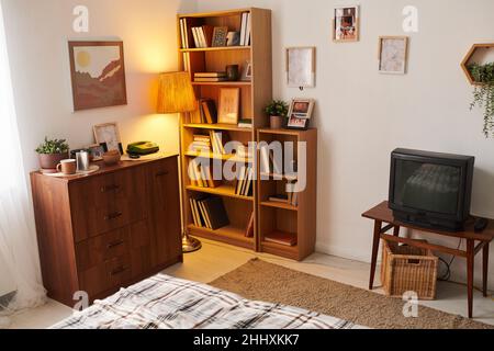 Partie de séjour ou chambre avec tv, étagères en bois avec livres, commode et tableaux dans un appartement moderne Banque D'Images