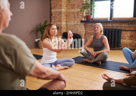 Jeune femme blonde moniteur de fitness consultant groupe de personnes âgées assis sur des tapis autour d'elle pendant la pause entre les entraînements Banque D'Images