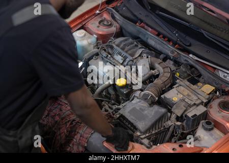 Partie de jeune mécanique dans l'usure de travail contrôle du moteur de voiture en se tenant par le capot ouvert avec le moteur Banque D'Images