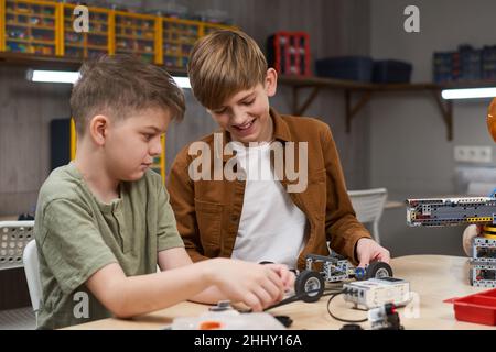 Deux garçons assis à la table et construisant une voiture à partir des détails du constructeur pendant la leçon de robotique Banque D'Images