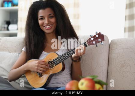 Bonne femme afro-américaine jouant sur ukulele dans le salon à la maison Banque D'Images