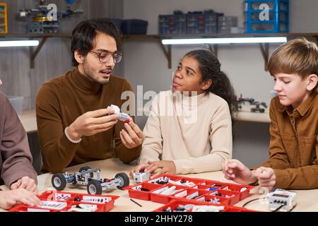 Jeune homme en lunettes assis à la table avec ses étudiants et leur enseignant la robotique Banque D'Images