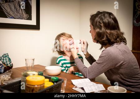 Une mère exécute un test d'antigène covid19 en insérant un écouvillon dans le nez de son jeune fils à la table de petit déjeuner avant l'école, à Amsterdam, aux pays-Bas. Banque D'Images