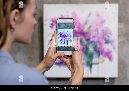 Gros plan d'une jeune femme qui fait de belles photos peintes sur le mur de son téléphone portable Banque D'Images