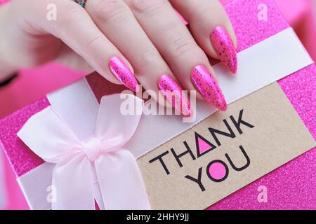 Les mains de femmes avec de longs ongles et vernis à ongles rose fluo tiennent une image avec l'inscription Merci Banque D'Images