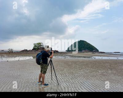 Photographe de la nature en action.Seul le voyageur tire le paysage marin avec un petit fond d'île.Backpacker prendre des photos sur la plage de sable à marée basse.FR Banque D'Images