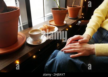 Service simple de cappuccino avec art floral en forme de cœur sur une table en bois sombre.Jean bleu d'une fille assise dans un café Banque D'Images