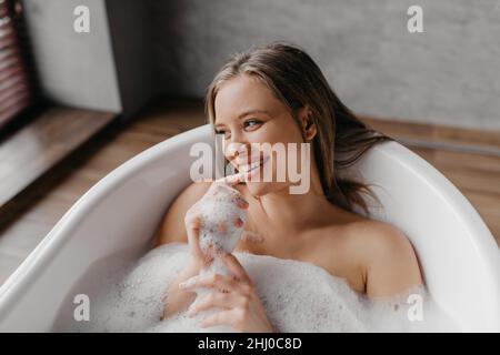 Bain relaxant.Bonne dame couchée dans la baignoire, appréciant le rituel de beauté et la mousse au spa de la maison, se reposant dans l'eau chaude à la maison Banque D'Images