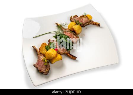 Côtelettes d'agneau grillées aux pommes de terre, aux épinards et aux herbes sur une assiette blanche isolée sur du blanc Banque D'Images