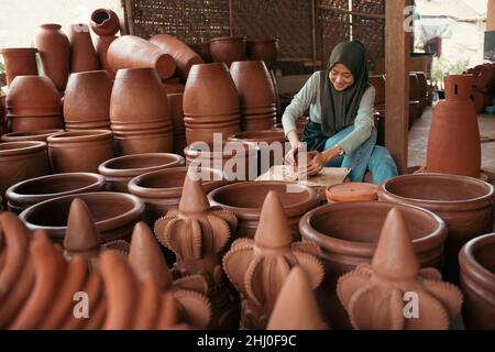 jeune femme en foulard assis travail d'argile parmi la poterie Banque D'Images