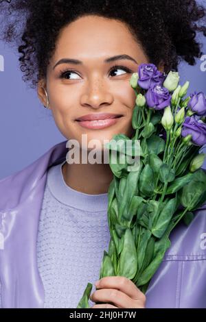 jeune femme afro-américaine rêveuse portant un bouquet de fleurs violettes isolées sur le violet Banque D'Images