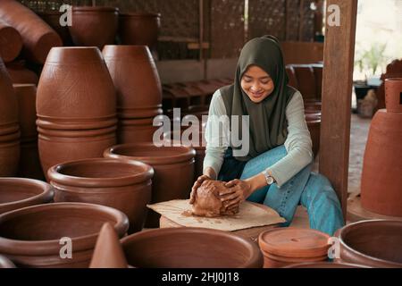 une jeune femme dans un hijab s'assoit à travailler l'argile dans la poterie Banque D'Images