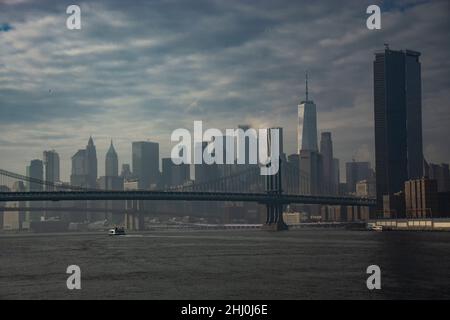 Dramatischer Blick von der Fähre auf dem East River auf die beiden Stahlbrücken und Lower Manhattan und dem imposanten One World Trade Center Banque D'Images