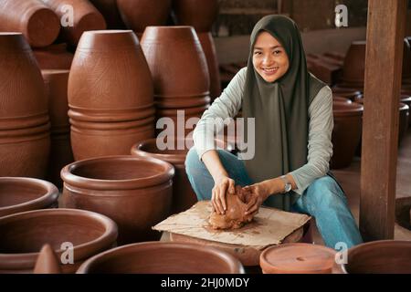 jeune femme souriante en foulard assis tranquillement parmi la poterie Banque D'Images