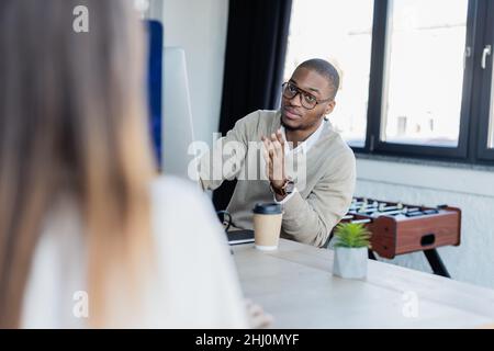 homme afro-américain en lunettes regardant une femme floue au bureau Banque D'Images