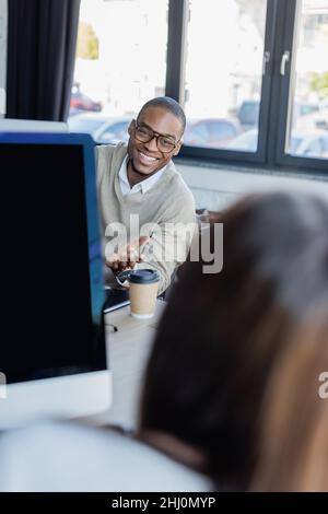 un homme afro-américain heureux en lunettes montrant une femme floue au bureau Banque D'Images