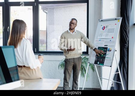 homme d'affaires afro-américain en lunettes montrant des graphiques à l'un de ses collègues avec une coupe de papier Banque D'Images