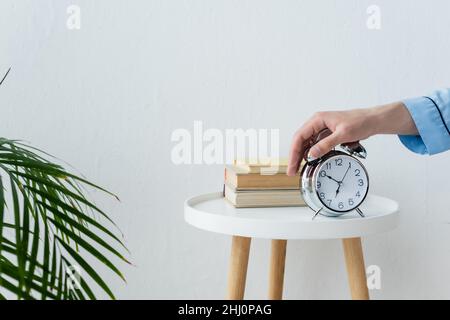 vue partielle de l'homme qui éteint le réveil vintage sur la table de chevet près des livres Banque D'Images