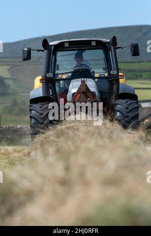 Exploitant agricole qui fait du foin de prairie traditionnel sur les hautes terres, avec un tracteur Hurlimann XL et une presse à balles carrées haute densité New Holland BB9060.Hawes, Yorkshire du Nord, U Banque D'Images