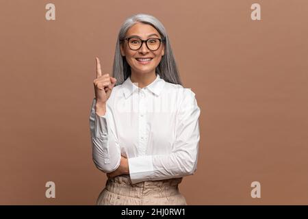 Asiatique belle femme mûre portant des lunettes et des vêtements formels a eu l'idée et elle a soulevé son doigt vers le haut.Studio isolé tourné sur fond beige Banque D'Images