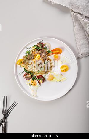 Pâtes à la dinde compotée, tomates cerises et herbes fraîches.Œufs de caille frits.Recettes délicieuses et saines de cuisine méditerranéenne.Vue de dessus.S vertical Banque D'Images