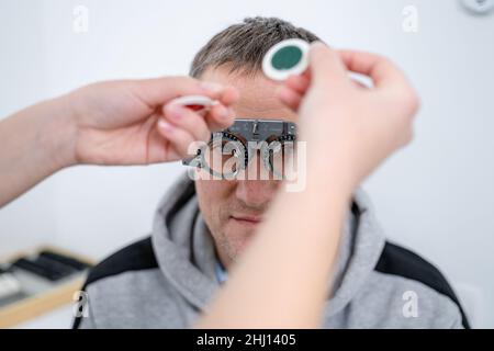 Correction de la vision.Sélection de lunettes.Des cadres d'essai professionnels sur le visage d'un patient mâle tandis que le médecin vérifie la vue chez un ophtalmologiste moderne Banque D'Images