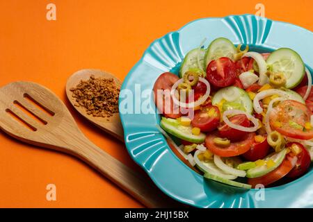 Goiania, Goias, Brésil – 25 janvier 2021 : une assiette avec salade de légumes et deux couverts en bois sur fond orange. Banque D'Images